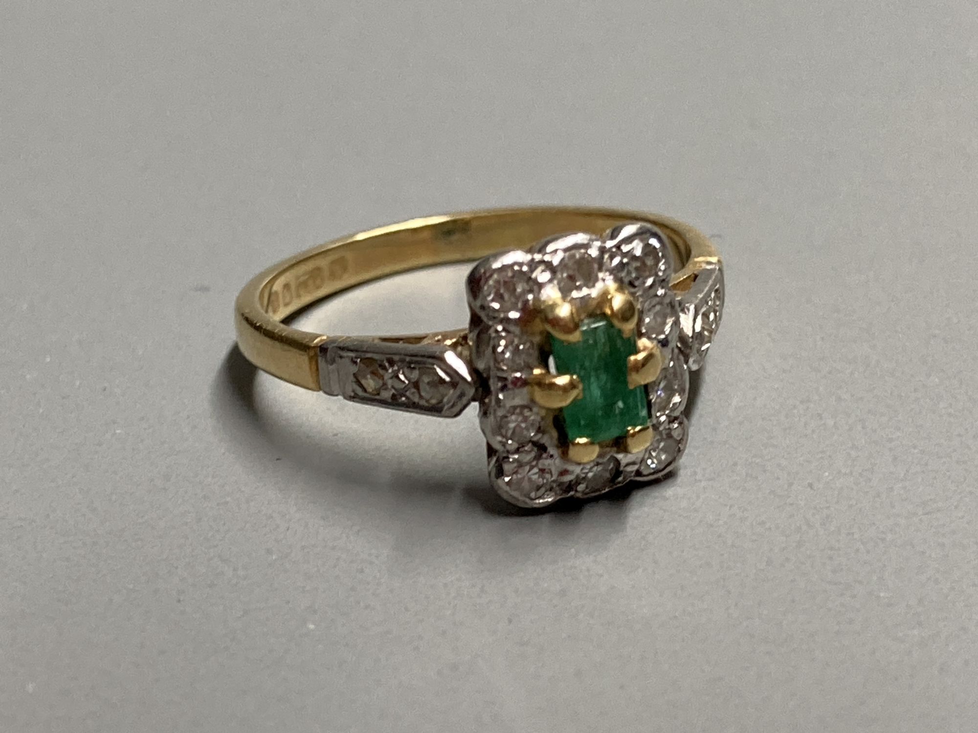 A modern 18ct gold, emerald and diamond rectangular cluster ring, with diamond set shoulders, size J, gross 2.7 grams.